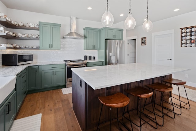 131 Owl Loop, Kalispell, MT 59901 - kitchen featuring appliances with stainless steel finishes, wall chimney range hood, wood finished floors, recessed lighting, and light stone counters