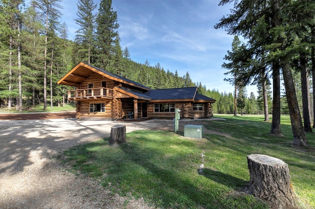 view of front facade with log siding, a view of trees, a front lawn, a wooden deck, and gravel driveway
