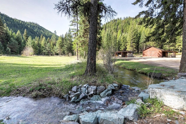 view of green lawn featuring a wooded view, an outbuilding, and a mountain view
