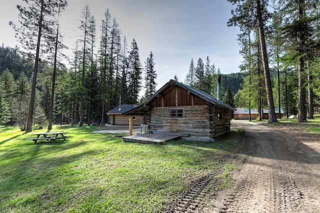 view of property exterior with log exterior, a wooden deck, a lawn, a view of trees, and dirt driveway