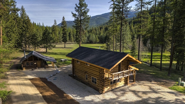 view of home's exterior with a wooded view, log exterior, a mountain view, gravel driveway, and a shingled roof