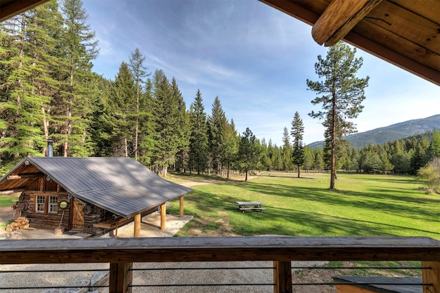 view of green lawn with a wooded view, a mountain view, and an outdoor structure