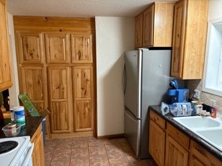 2225 Pattee Canyon Rd, Missoula, MT 59803 - kitchen with freestanding refrigerator, light tile patterned floors, brown cabinets, and dark countertops