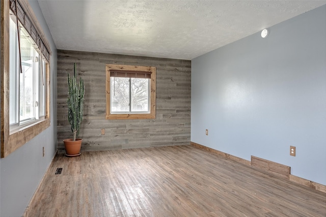 unfurnished room with wood finished floors, healthy amount of natural light, baseboards, wooden walls, and a textured ceiling