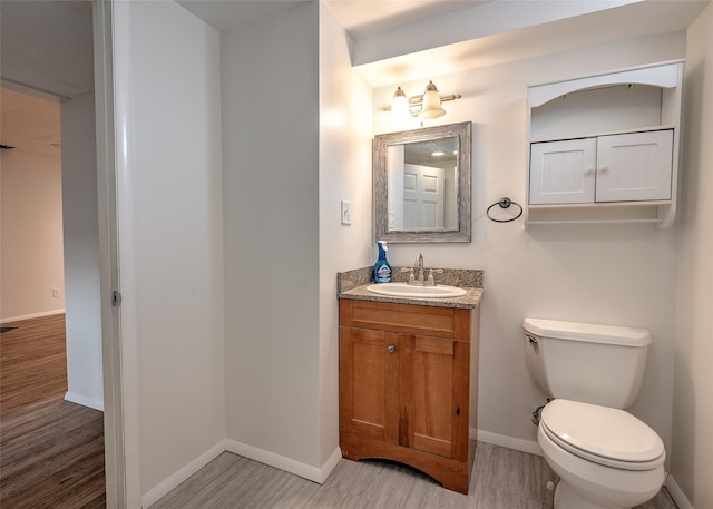 half bathroom with toilet, vanity, wood finished floors, and baseboards
