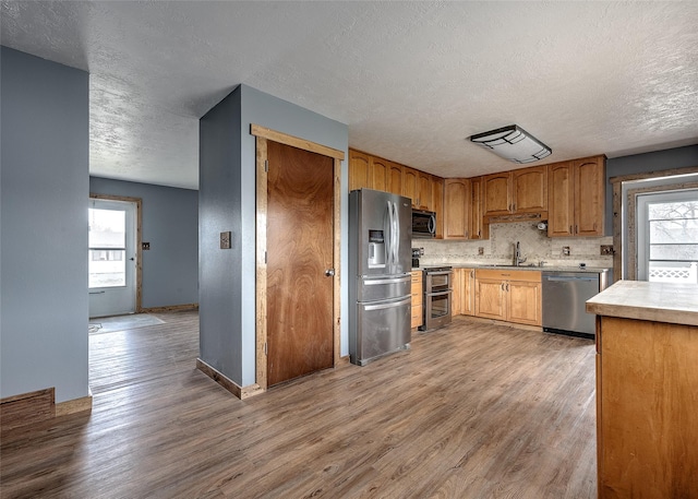 kitchen with stainless steel appliances, a textured ceiling, wood finished floors, light countertops, and a sink