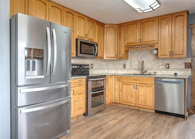 kitchen featuring appliances with stainless steel finishes, a sink, light wood-type flooring, tasteful backsplash, and light stone countertops