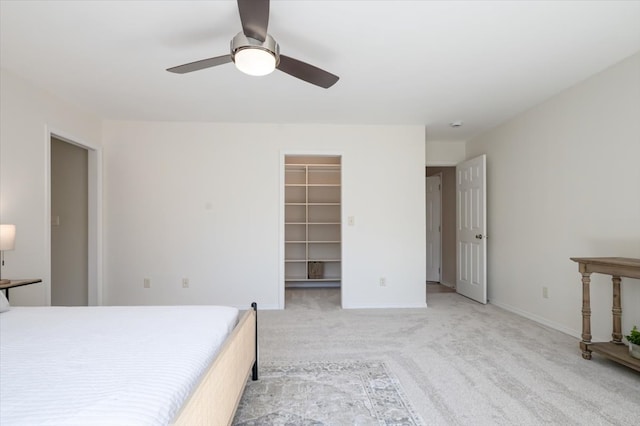 unfurnished bedroom with light carpet, a ceiling fan, a spacious closet, and baseboards