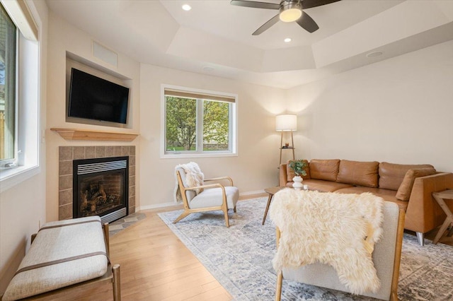 living area featuring a fireplace, ceiling fan, a raised ceiling, light wood-style floors, and recessed lighting