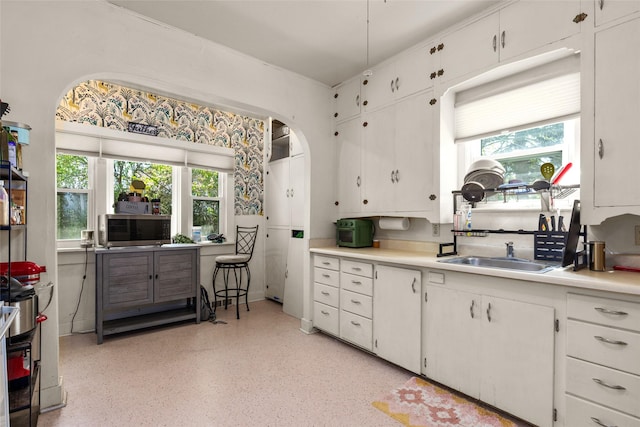528 3rd Ave E, Kalispell, MT 59901 - kitchen featuring a sink, light countertops, dark speckled floor, white cabinets, and arched walkways