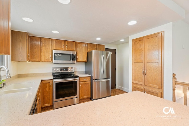kitchen featuring appliances with stainless steel finishes, a sink, recessed lighting, brown cabinetry, and light wood-type flooring