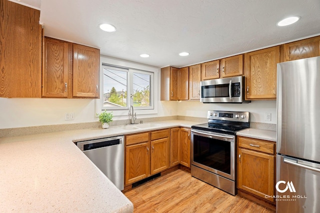 kitchen with stainless steel appliances, a sink, light countertops, light wood-style floors, and recessed lighting