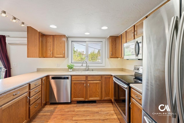kitchen featuring appliances with stainless steel finishes, a sink, light wood-style flooring, light countertops, and brown cabinets