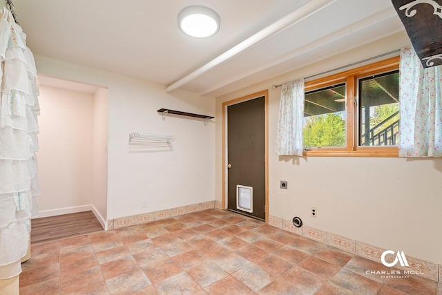 clothes washing area with hookup for an electric dryer, baseboards, and stone finish floors