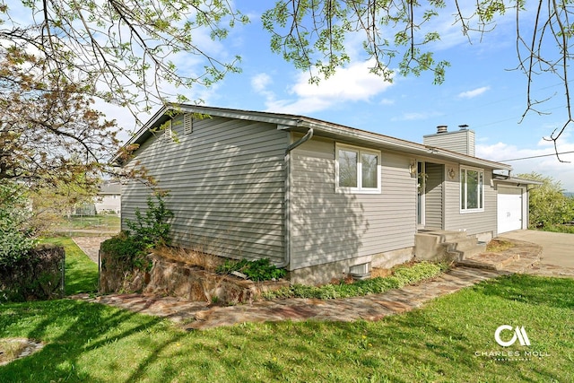 view of side of property featuring a lawn, a chimney, driveway, and a garage