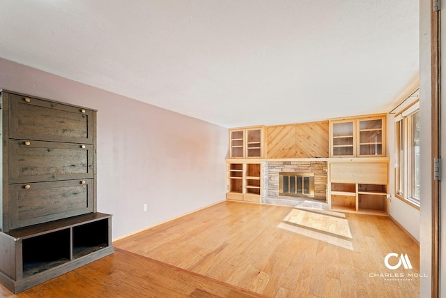 unfurnished living room with wood finished floors, baseboards, and a stone fireplace