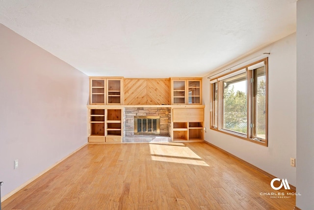 unfurnished living room with wood finished floors, baseboards, a stone fireplace, and built in shelves