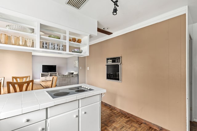 kitchen with tile countertops, electric cooktop, white cabinets, baseboards, and stainless steel oven