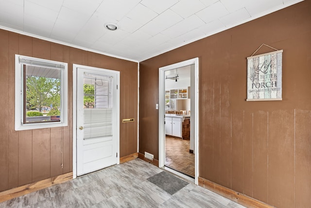 entryway featuring ornamental molding, wooden walls, and baseboards