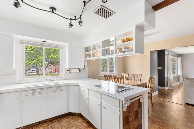 kitchen featuring open shelves, a sink, tile countertops, black electric stovetop, and a peninsula