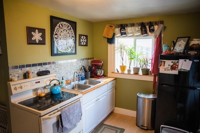 kitchen featuring white electric range oven, freestanding refrigerator, a sink, white cabinets, and light wood-style flooring