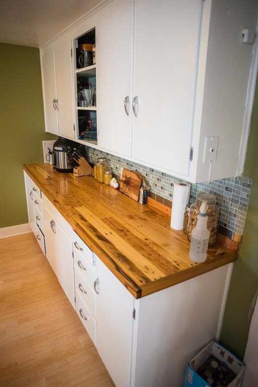 kitchen with white cabinetry, light wood-type flooring, decorative backsplash, and baseboards