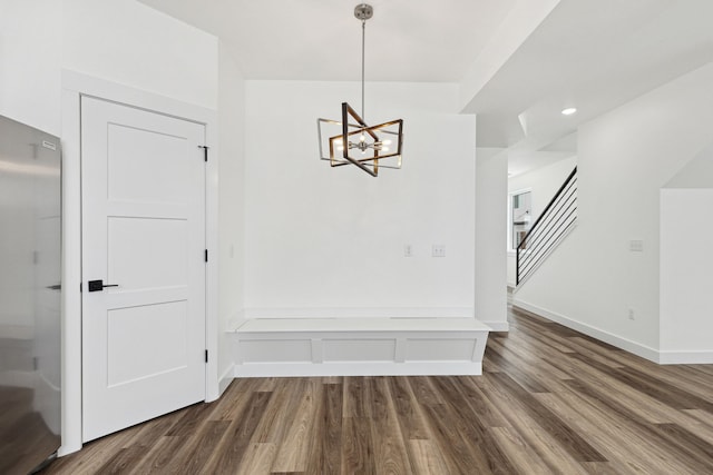 unfurnished dining area featuring dark wood-style floors, a chandelier, stairway, and baseboards