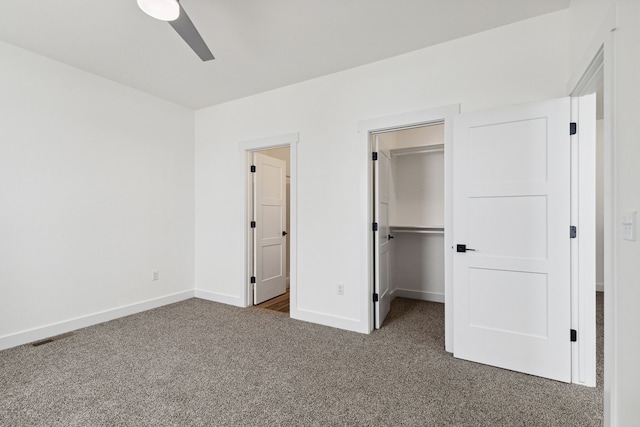 unfurnished bedroom with carpet, a spacious closet, baseboards, ceiling fan, and a closet