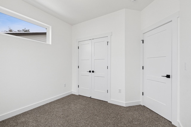 unfurnished bedroom with dark colored carpet, baseboards, and a closet