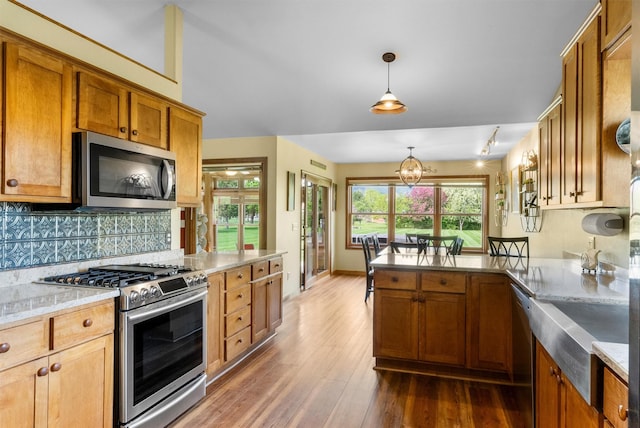 1815 Homestead Dr, Missoula, MT 59808 - kitchen featuring appliances with stainless steel finishes, a peninsula, wood finished floors, decorative backsplash, and brown cabinetry