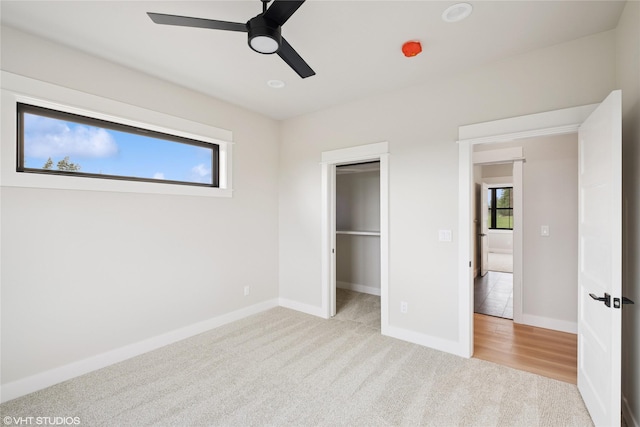 unfurnished bedroom featuring light carpet, baseboards, ceiling fan, and a walk in closet