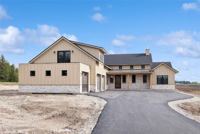 modern farmhouse featuring a standing seam roof, board and batten siding, stone siding, asphalt driveway, and metal roof