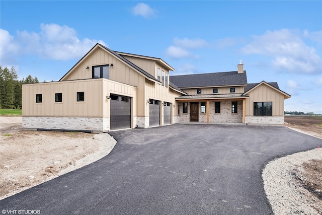 view of front facade with a standing seam roof, stone siding, board and batten siding, driveway, and metal roof
