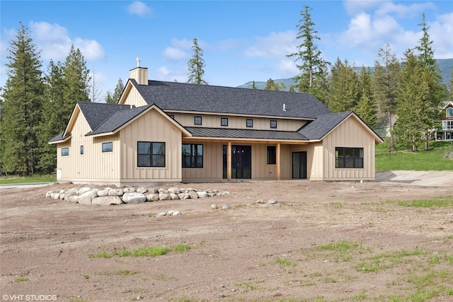 modern farmhouse style home featuring board and batten siding, a shingled roof, a standing seam roof, a chimney, and metal roof
