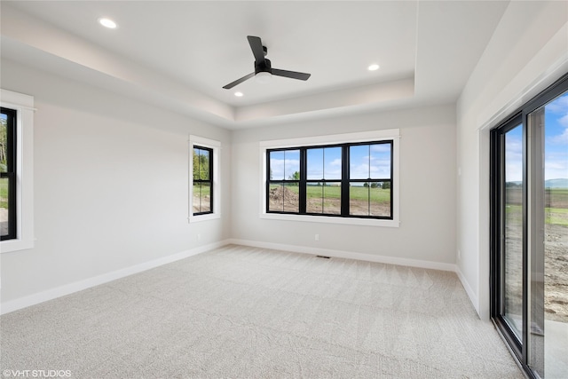 empty room with carpet flooring, a tray ceiling, baseboards, recessed lighting, and ceiling fan