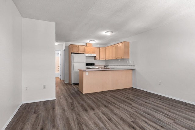 kitchen with dark wood-style floors, a peninsula, light brown cabinetry, a sink, and freestanding refrigerator