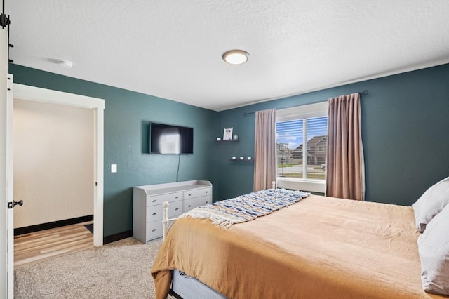 bedroom featuring a textured ceiling, light carpet, baseboards, and a textured wall