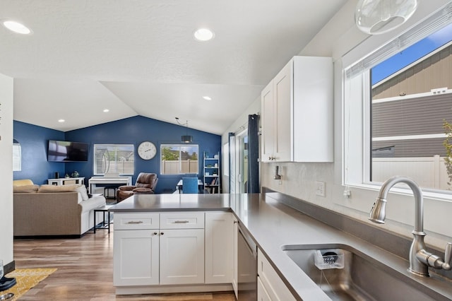 kitchen with a sink, a peninsula, vaulted ceiling, white cabinets, and dishwasher