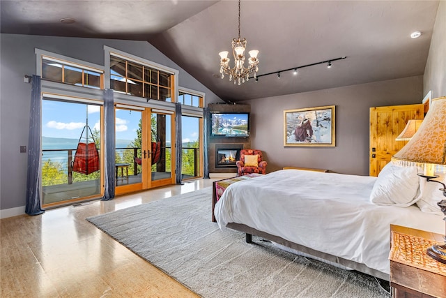 32220 Tamarack Dr, Bigfork, MT 59911 - bedroom with access to exterior, lofted ceiling, a chandelier, multiple windows, and a glass covered fireplace