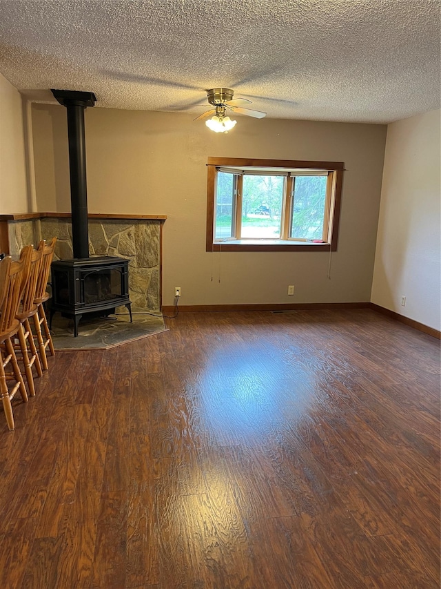 156 Clary Ave W, Geraldine, MT 59446 - unfurnished living room featuring a wood stove, wood finished floors, a textured ceiling, baseboards, and a ceiling fan