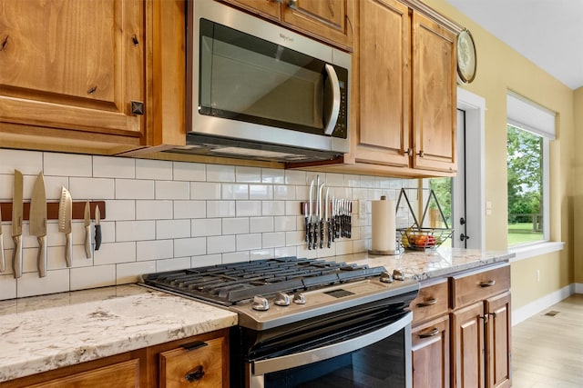 500 Bass Ln, Corvallis, MT 59828 - kitchen with stainless steel appliances, brown cabinetry, backsplash, light stone counters, and baseboards