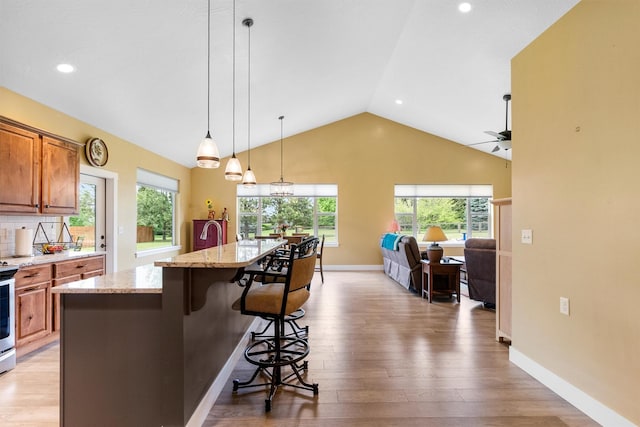 500 Bass Ln, Corvallis, MT 59828 - kitchen featuring brown cabinets, lofted ceiling, light stone counters, light wood-style flooring, and a kitchen bar