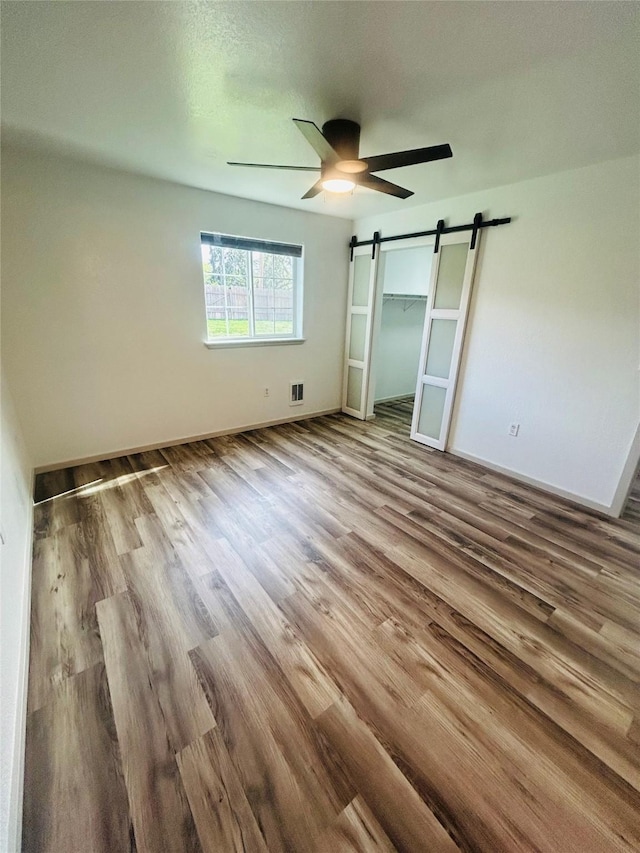 4 Weber Ave, Polson, MT 59860 - unfurnished bedroom featuring a barn door, wood finished floors, ceiling fan, and baseboards