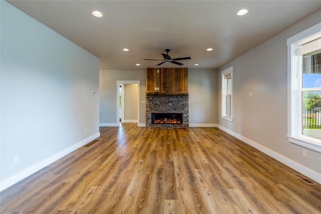 unfurnished living room with baseboards, recessed lighting, ceiling fan, wood finished floors, and a stone fireplace