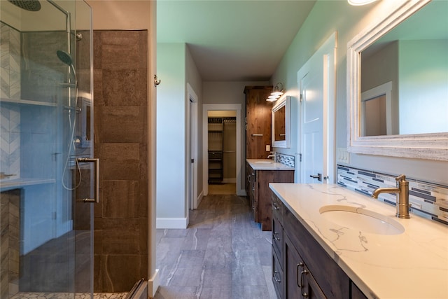 bathroom featuring a shower stall, two vanities, a walk in closet, decorative backsplash, and baseboards