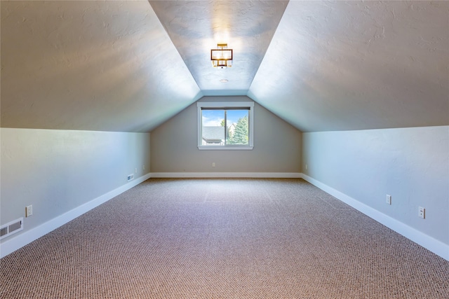 additional living space with carpet, vaulted ceiling, baseboards, and a textured ceiling