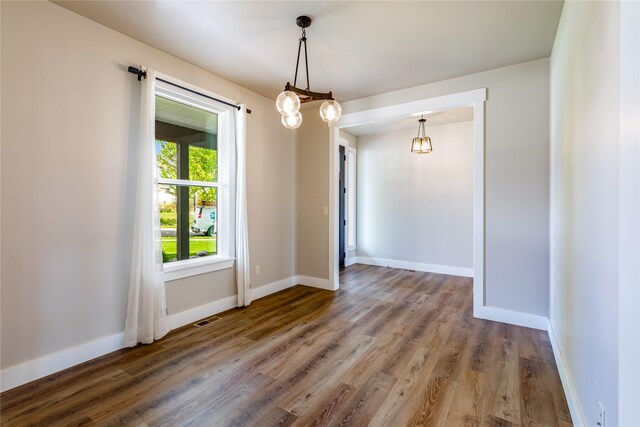 unfurnished room featuring wood finished floors, baseboards, and a chandelier