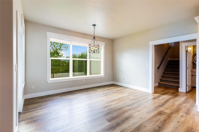 unfurnished dining area with a chandelier, stairs, light wood-type flooring, and baseboards