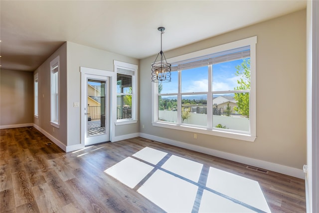 unfurnished dining area featuring a chandelier, healthy amount of natural light, baseboards, and wood finished floors