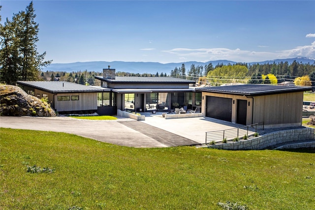 view of front of home featuring concrete driveway, a front yard, a mountain view, a chimney, and a porch